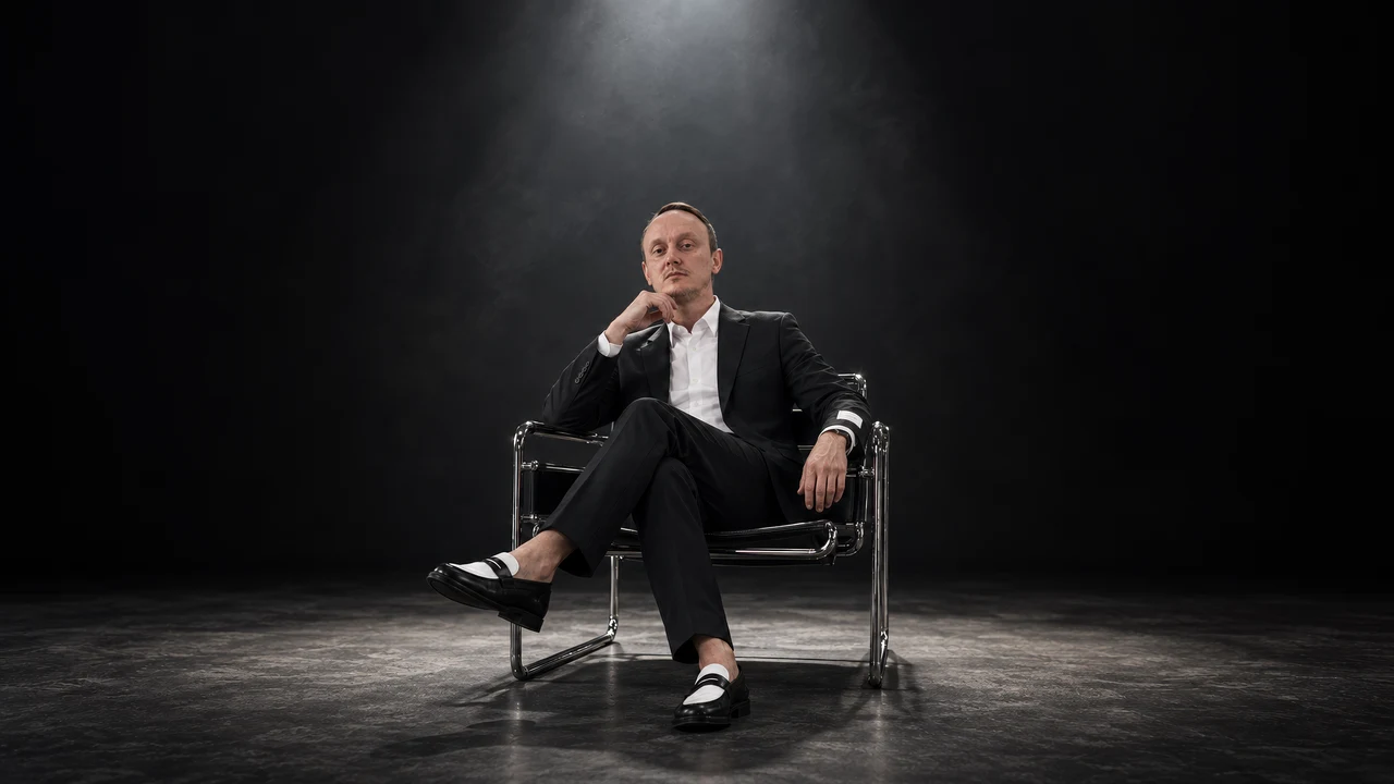 Ivan sedi na stolici u tamnom studiju i gleda pravo u kameru.